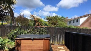 A hot tub in a backyard with a wooden deck, surrounded by a fence and greenery.