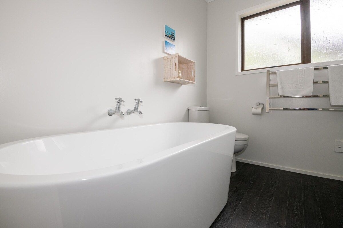 Een moderne badkamer met een vrijstaand bad, een toilet en een raam.