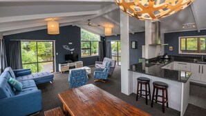 A modern living room with a sofa, a wooden table, and a kitchen area with a bar counter and stools.