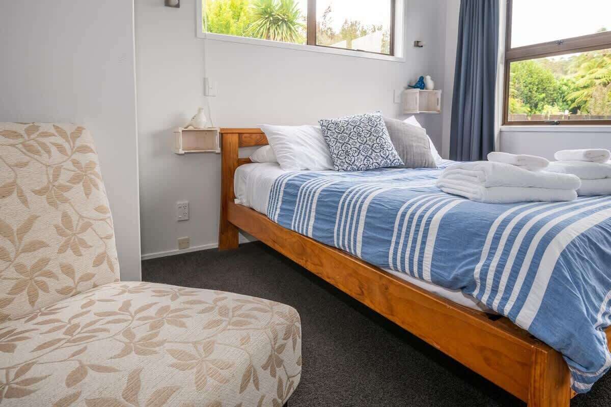 Een slaapkamer met een bed, nachtkastje, stoel en een raam met uitzicht op groen.