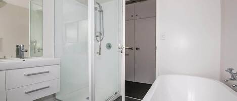 Une salle de bain moderne avec une douche à parois de verre, une baignoire blanche et un meuble-lavabo avec des tiroirs.