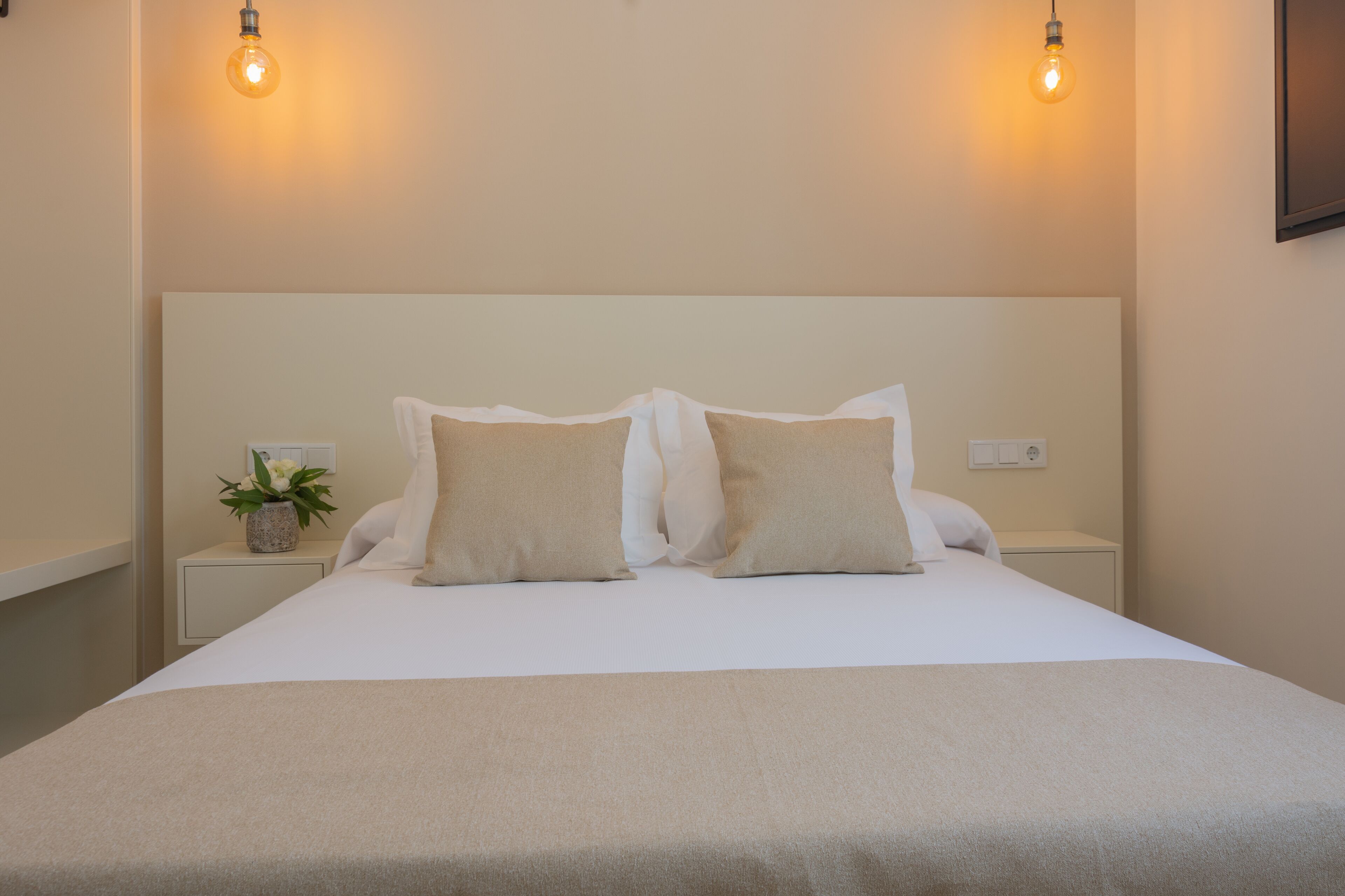 Una cama bien hecha con dos almohadas y una mesita de noche con una planta.