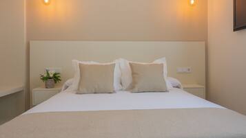 Una cama bien hecha con dos almohadas y una mesita de noche con una planta.