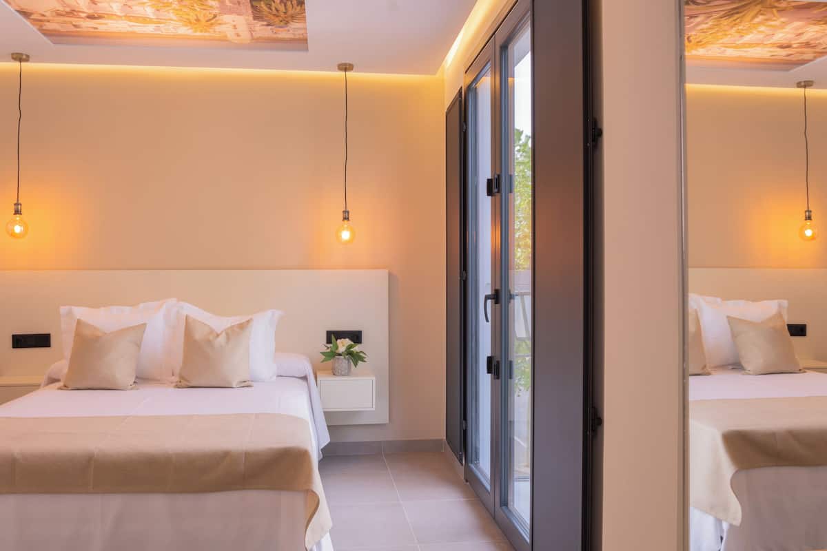 A modern bedroom with two beds, a bedside table with a vase, and a large window.