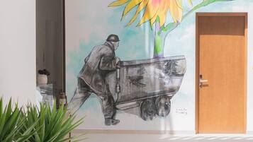 Un mural con un girasol y un hombre empujando un carrito, una puerta de madera y plantas en macetas en un pasillo.