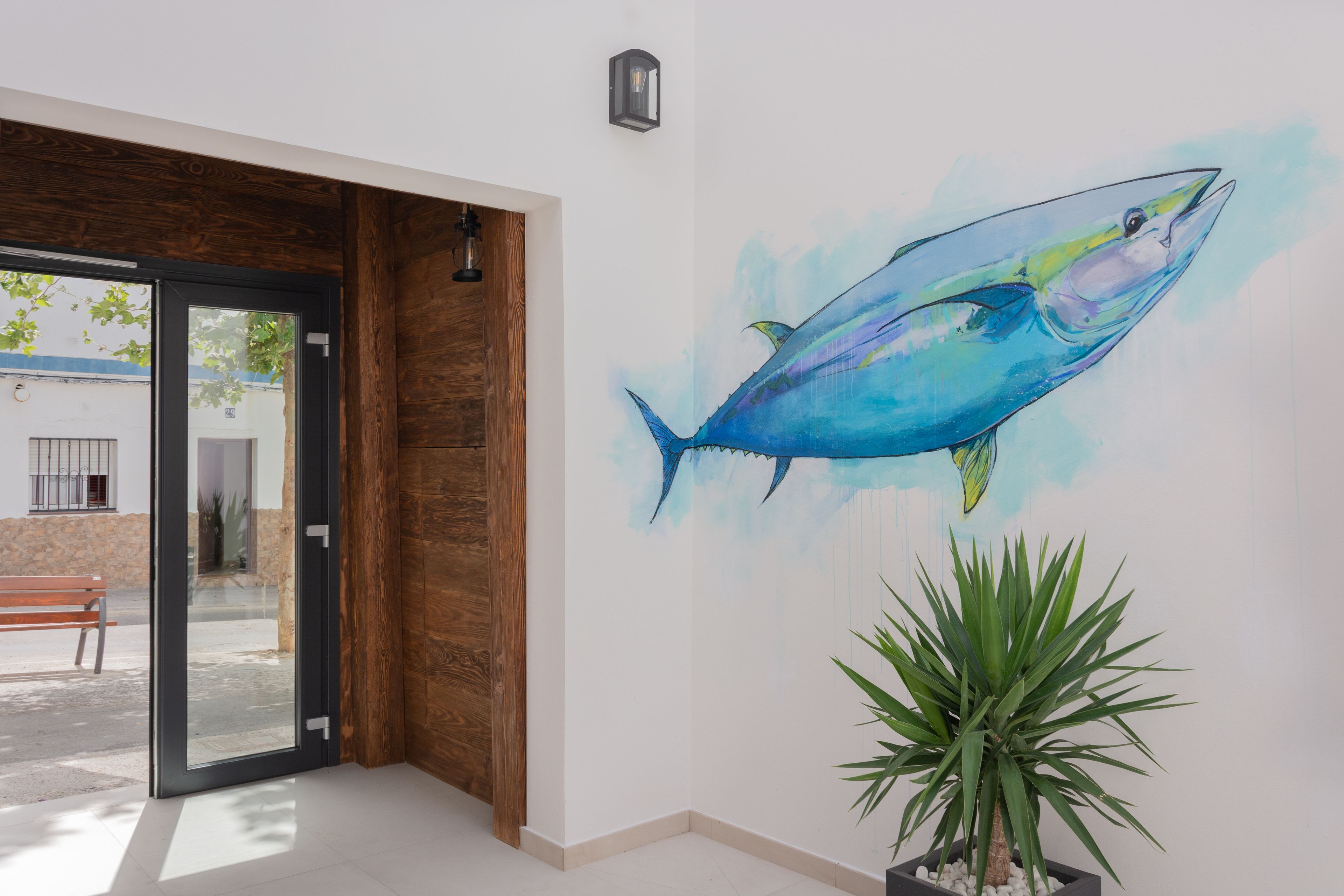 Une pièce avec une porte en bois, une plante en pot et une fresque murale représentant un poisson.