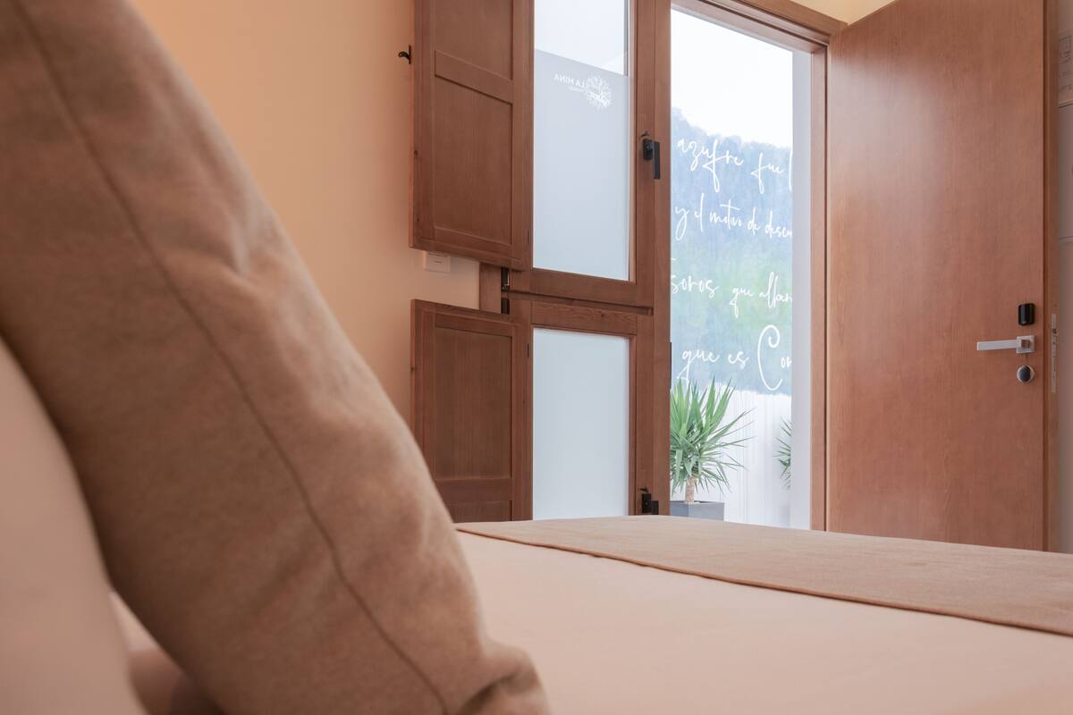 A bedroom with a bed, wooden wardrobe, and a view of a mountain through a glass door.