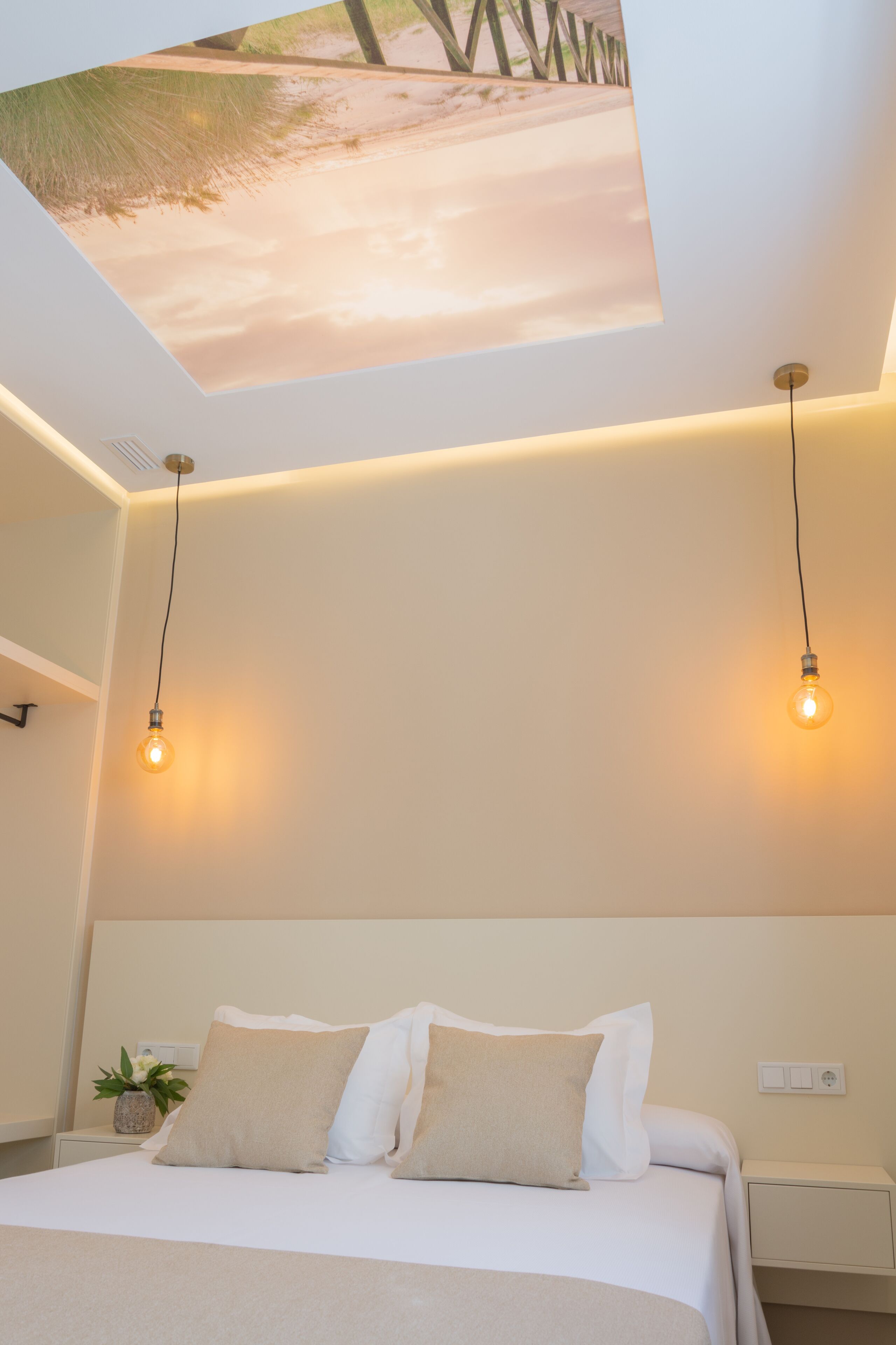 Une chambre d’hôtel moderne équipée d’un lit, de deux lampes de chevet, d’une table de nuit et d’une fresque murale représentant une scène de plage.
