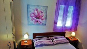 A bedroom with a bed, two bedside tables with lamps, a painting of a flower, and a window with purple curtains. - Apartment in Sevid with Seaview, Balcony, Air condition, WIFI (4755-3) (Sevid)