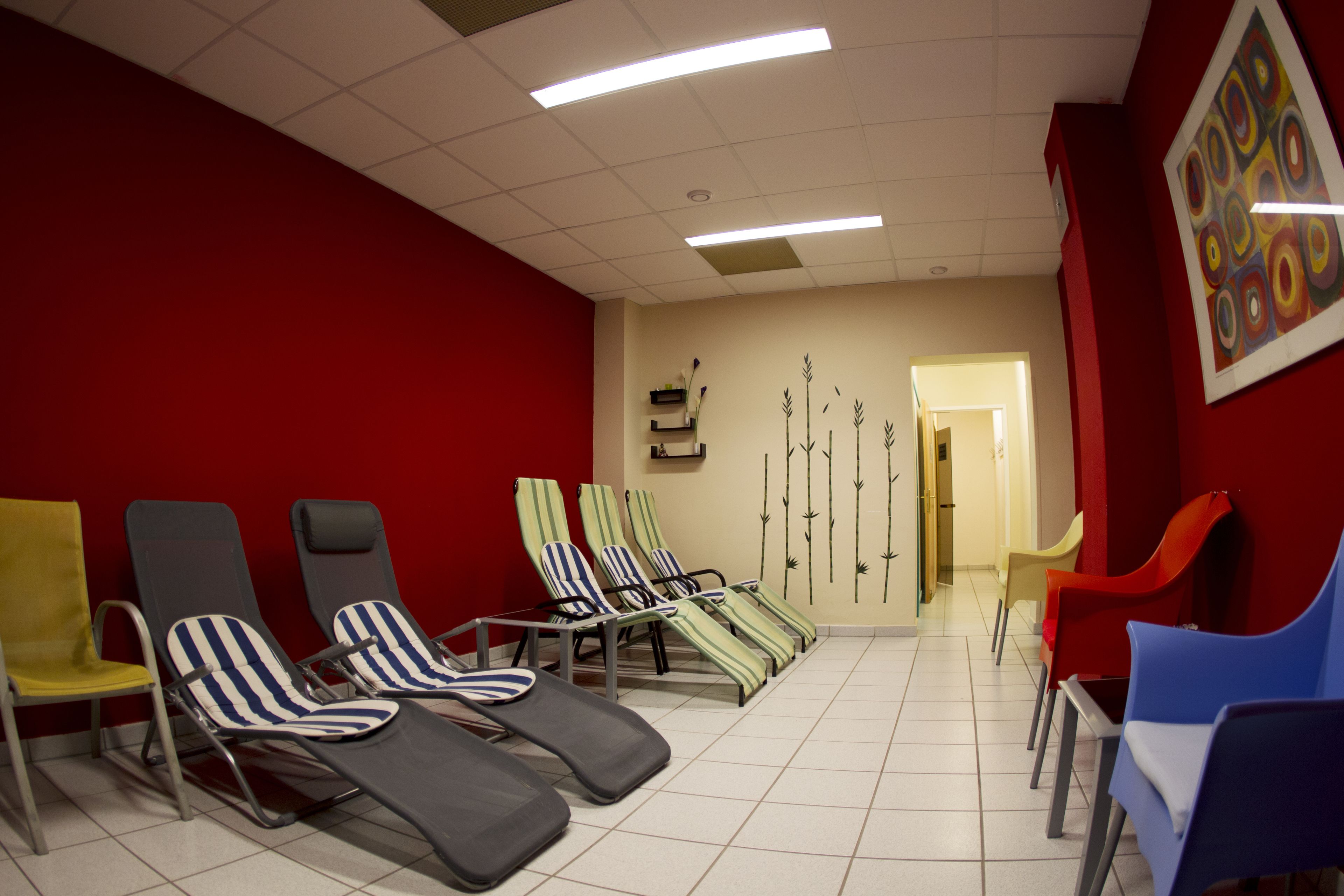 Une pièce dotée de plusieurs chaises longues et de fauteuils, d’un mur rouge et d’une porte donnant sur une autre pièce.