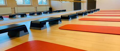 Ein Fitnessraum mit Trainingsgeräten, Matten und einer Spiegelwand.