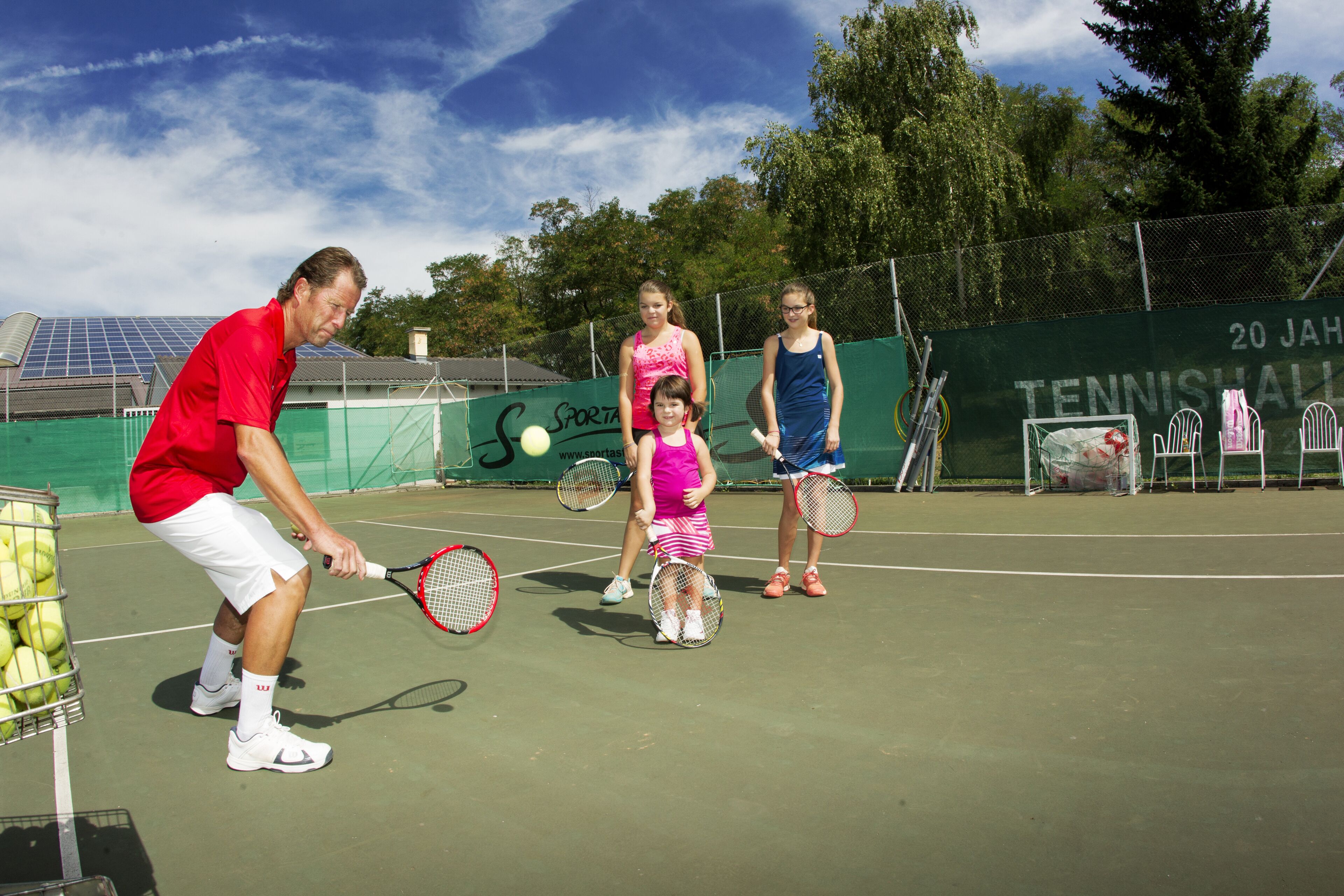 En tennisbane med net, hegn og træer i baggrunden.