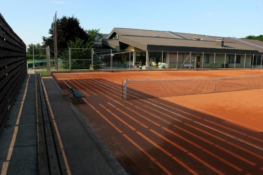 Una cancha de tenis con red, bancos y un edificio con techo.