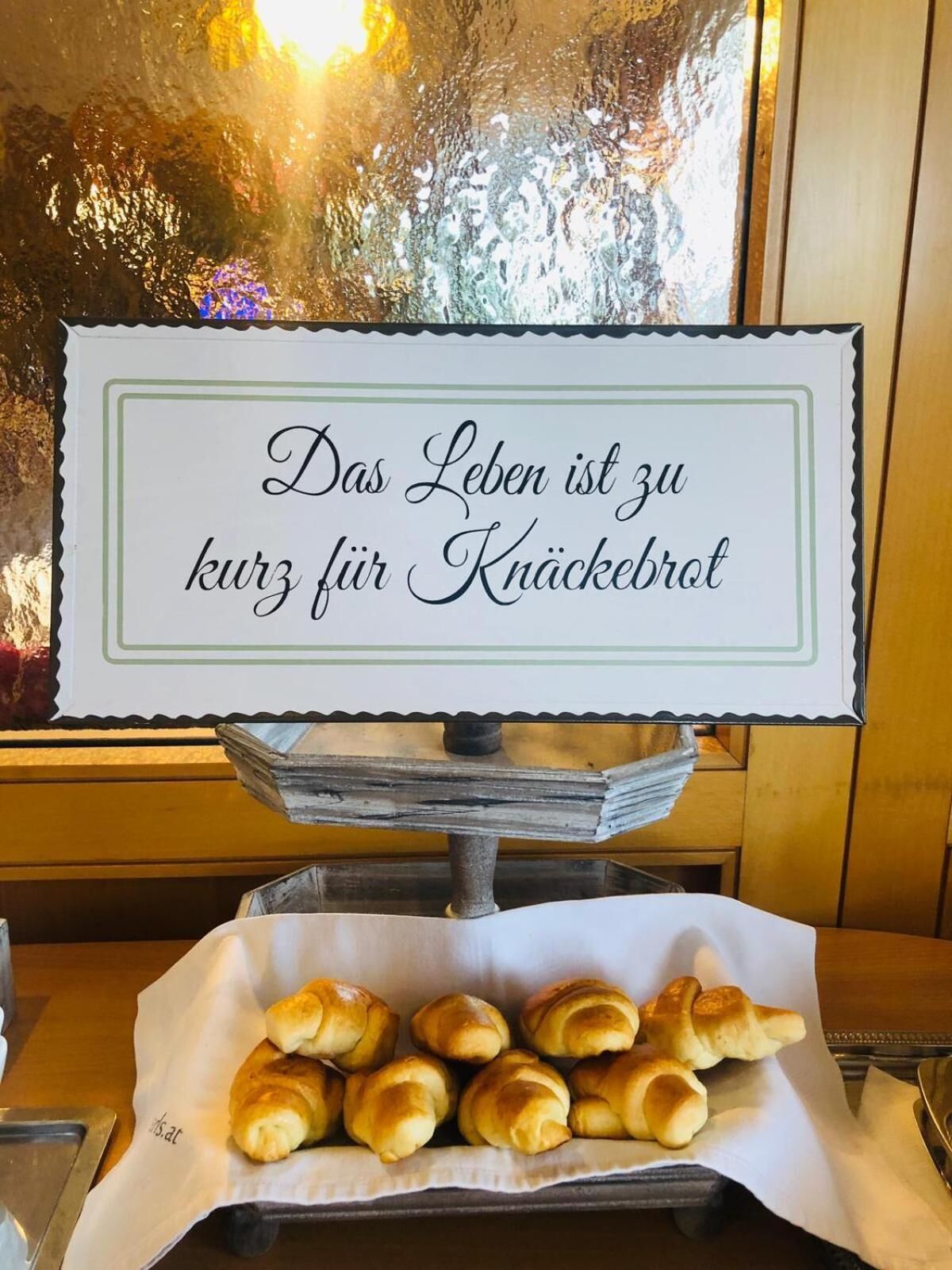 A sign with a message in German, a tray with bread rolls, and a window with a view.