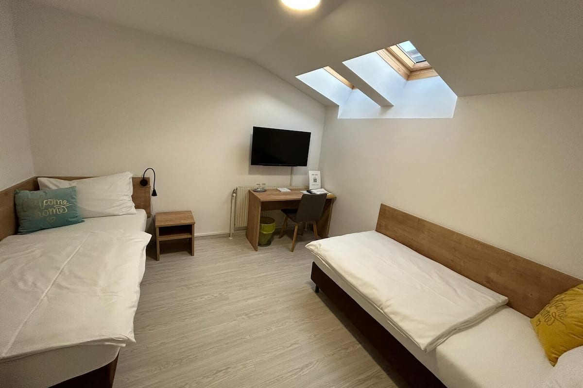 Ein Schlafzimmer mit zwei Betten, einem Schreibtisch, einem Stuhl, einem Fernseher und Dachfenstern.