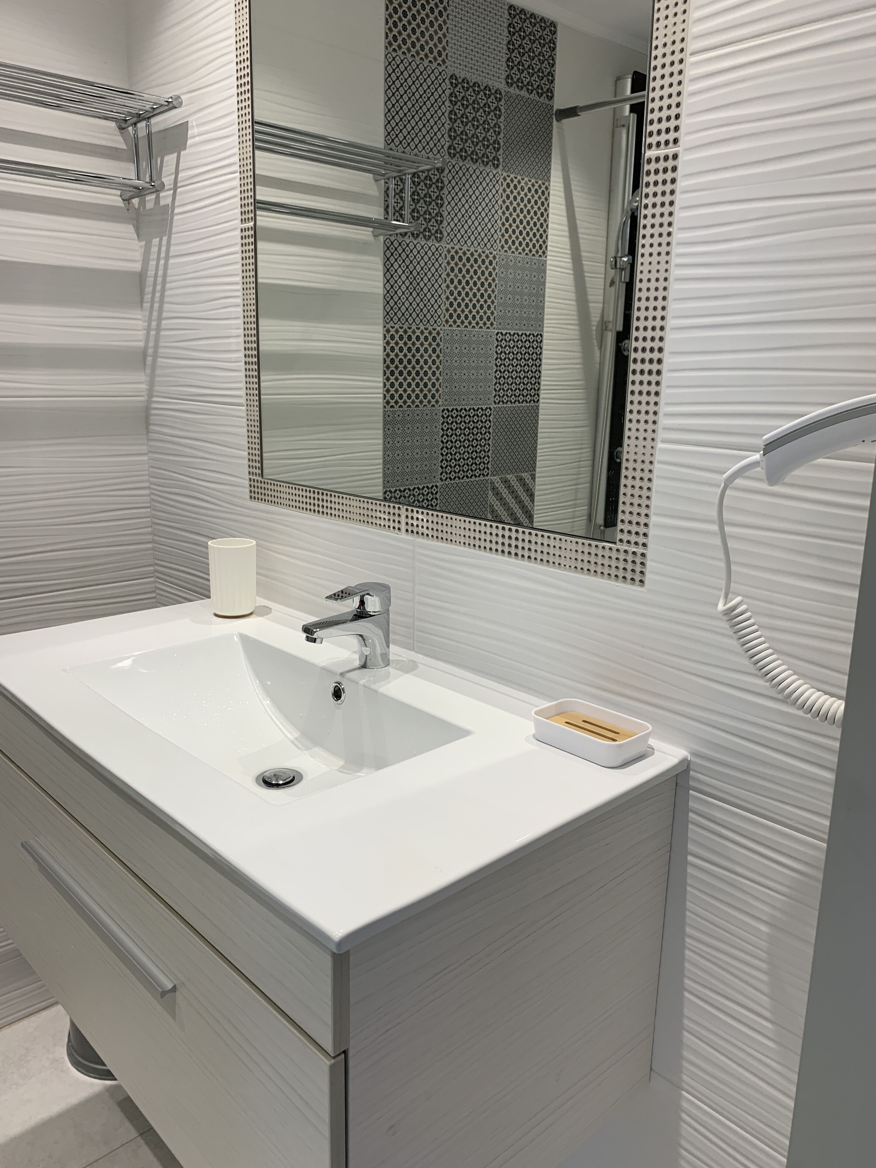 A modern bathroom with a white vanity, a large mirror, and a shower area.