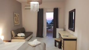 A hotel room with a bed, a sofa, a desk, and a view of the sea. - Dioni Hotel (Rethymno)