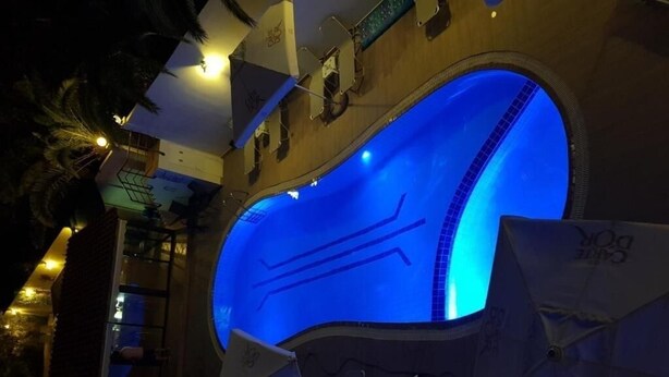 A swimming pool with a blue illuminated interior, surrounded by umbrellas and a wooden deck. - Dioni Hotel (Rethymno)