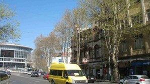 Straßenszene mit einem gelben Lieferwagen, Gebäuden und Bäumen.