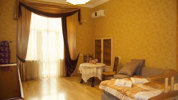 Ein Hotelzimmer mit Bett, einem kleinen Tisch mit einer Vase, einem Sessel und einem Fenster mit Vorhängen.