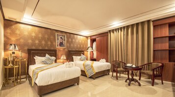 A hotel room with two beds, a sitting area with a table and chairs, and a wardrobe.
