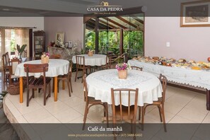 A cozy dining area with round tables and chairs, a buffet setup, and a stone fireplace. - Pousada Casa de Pedra (Blumenau)