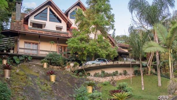 Una casa con techo inclinado, una escalera de piedra y un coche aparcado delante.