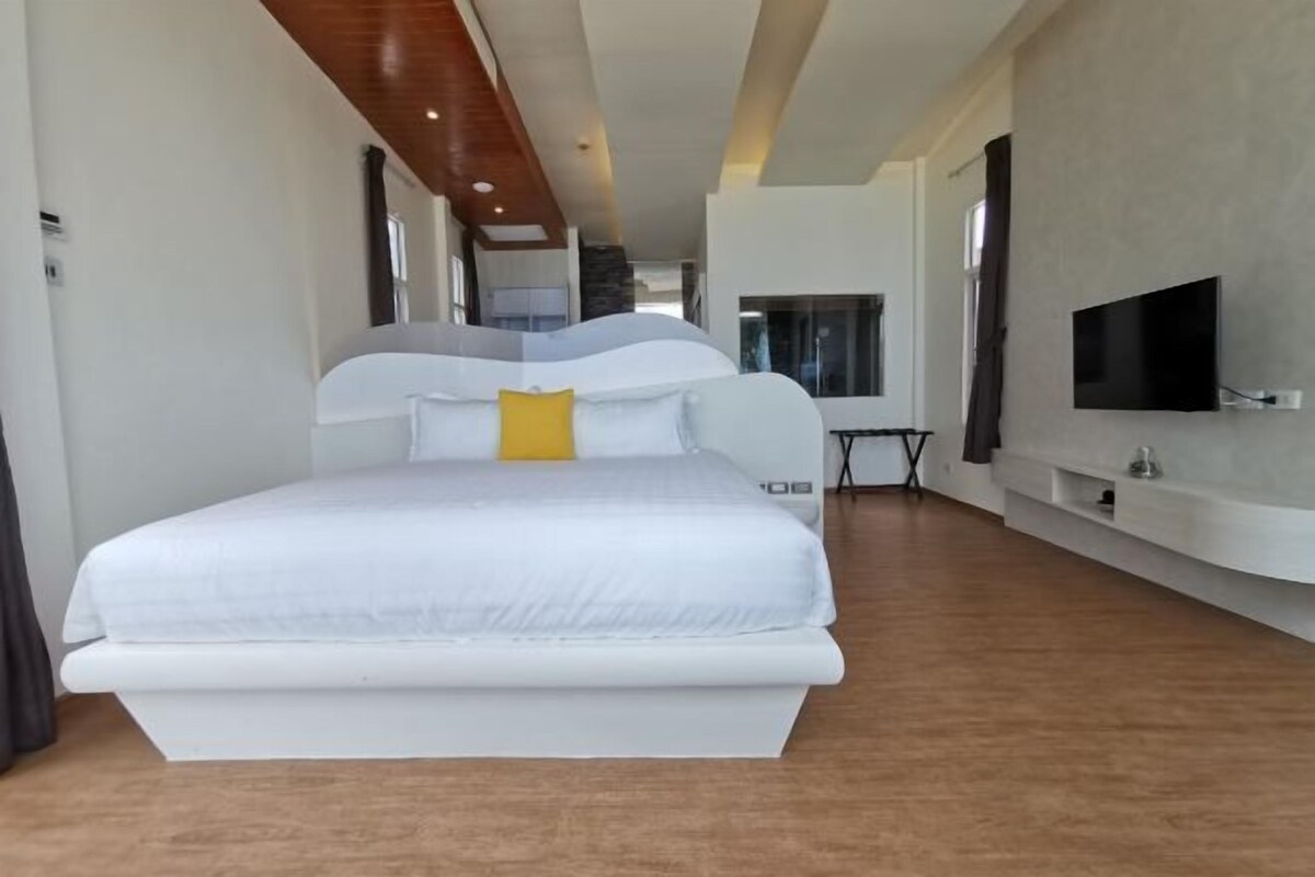Une chambre à coucher moderne avec un grand lit, un téléviseur à écran plat fixé au mur et un plafond en bois.