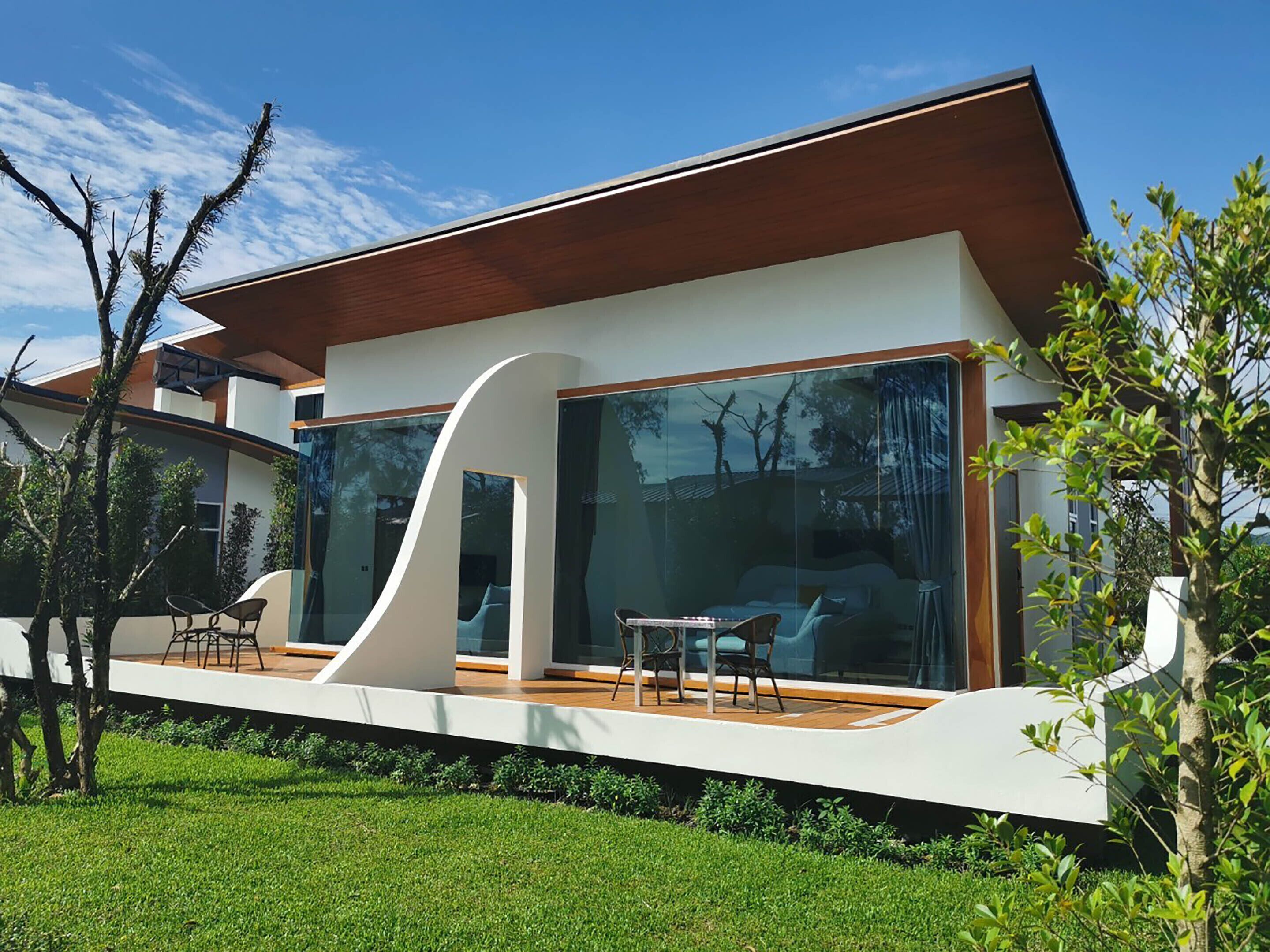 Una casa moderna con amplios ventanales de vidrio, una terraza de madera y un césped cuidado.