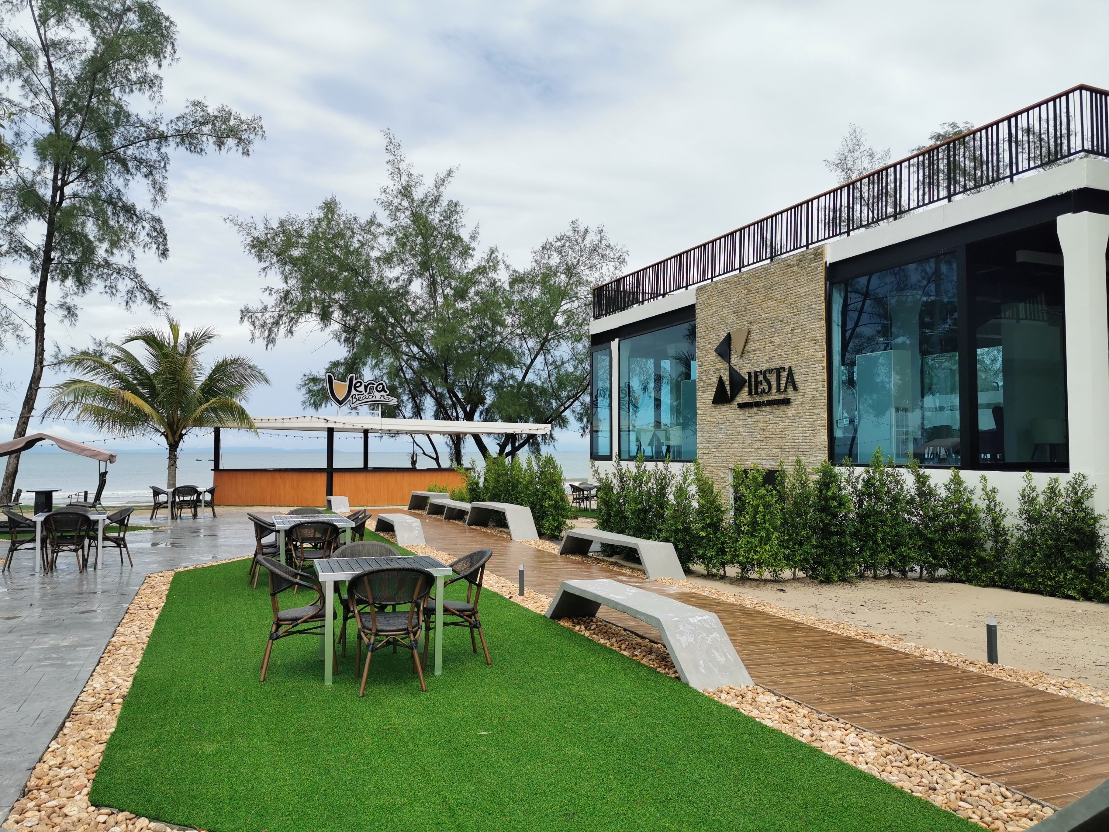 An outdoor seating area with tables and chairs, a wooden deck, and a view of the sea.