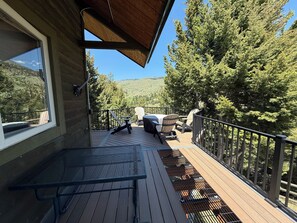 Una terrassa de fusta amb una taula de metall i dues cadires Adirondack, amb vista a una vessant boscosa.