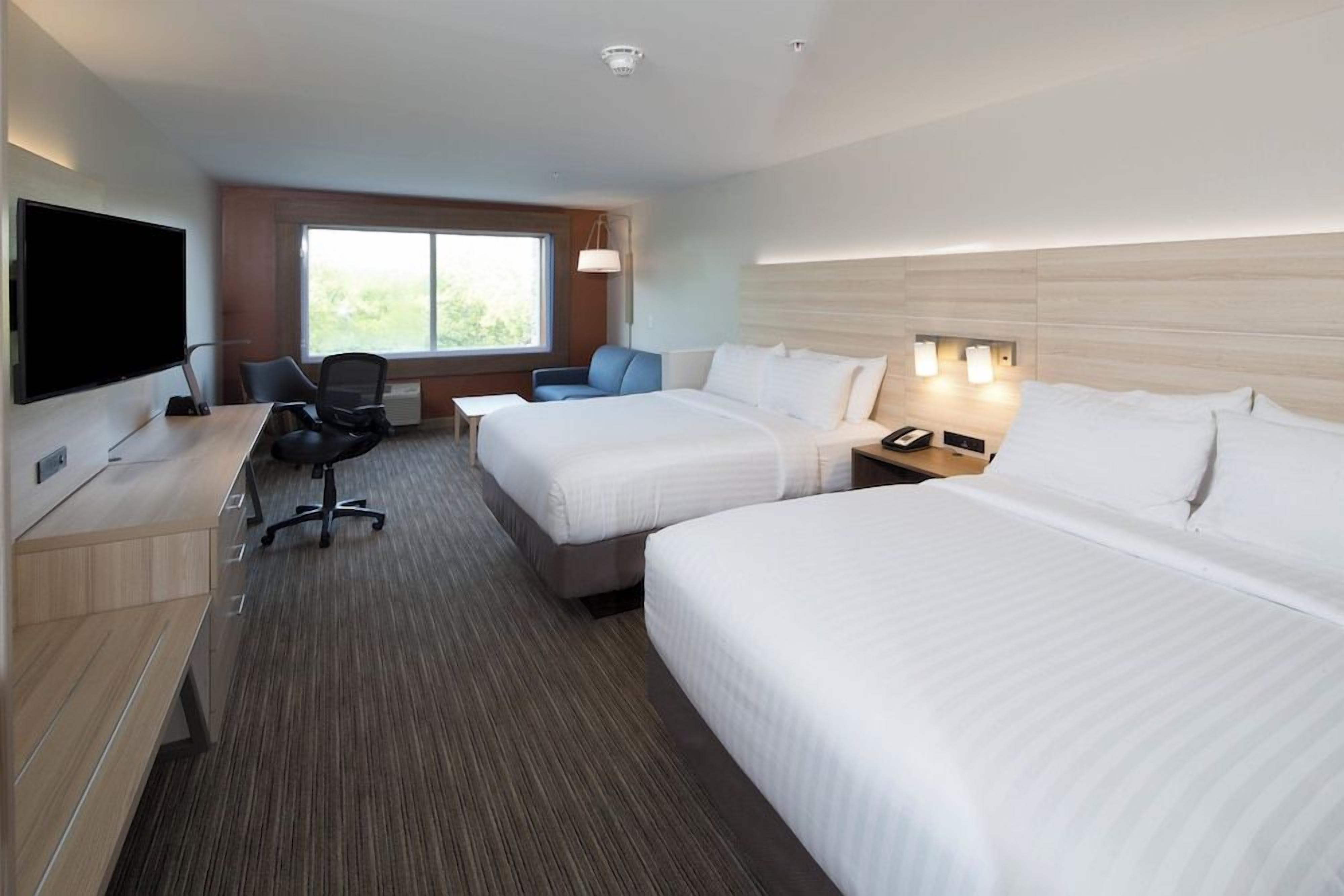 A hotel room with two beds, a desk with a chair, a TV, and a window with a view.