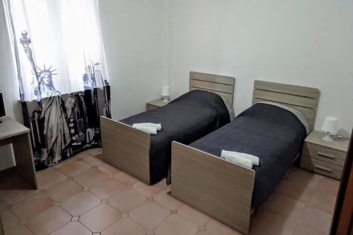 A room with two beds, each with a wooden headboard and a small bedside table with a lamp.