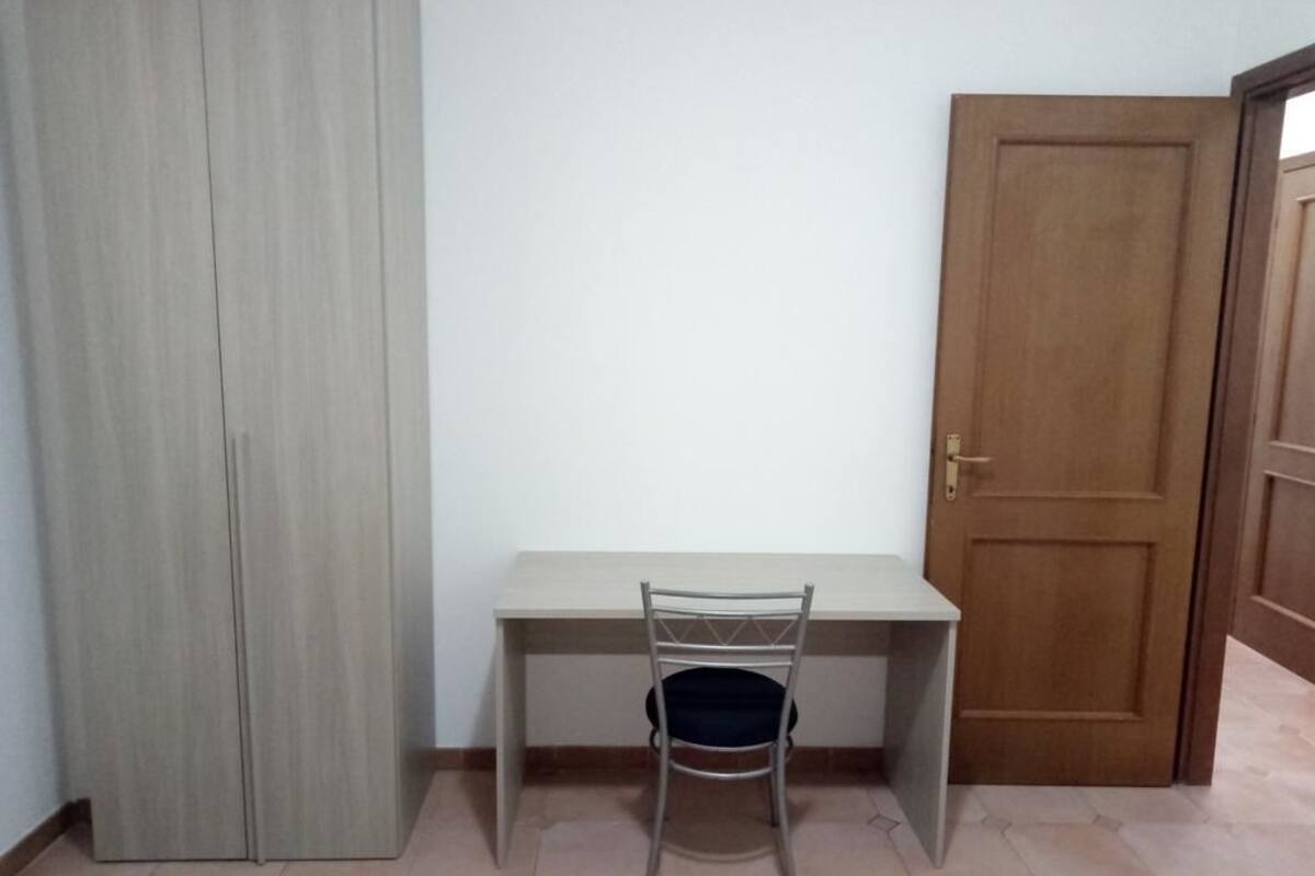 A room with a wooden door, a white desk, and a metal chair.