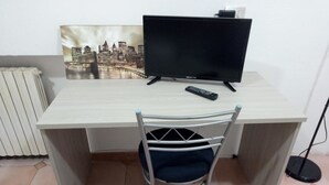 Una habitación con escritorio, silla, televisor y control remoto.