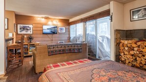 A cozy bedroom with a large bed, a wooden desk, a chair, a TV mounted on the wall, and a fireplace. - Cozy Mammoth Studio – Fireplace, Pets Welcome (Mammoth Lakes)