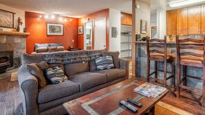 A cozy living room with a fireplace, a sofa with patterned cushions, a coffee table with magazines, and wooden chairs. - Cozy Mammoth Studio – Fireplace, Pets Welcome (Mammoth Lakes)