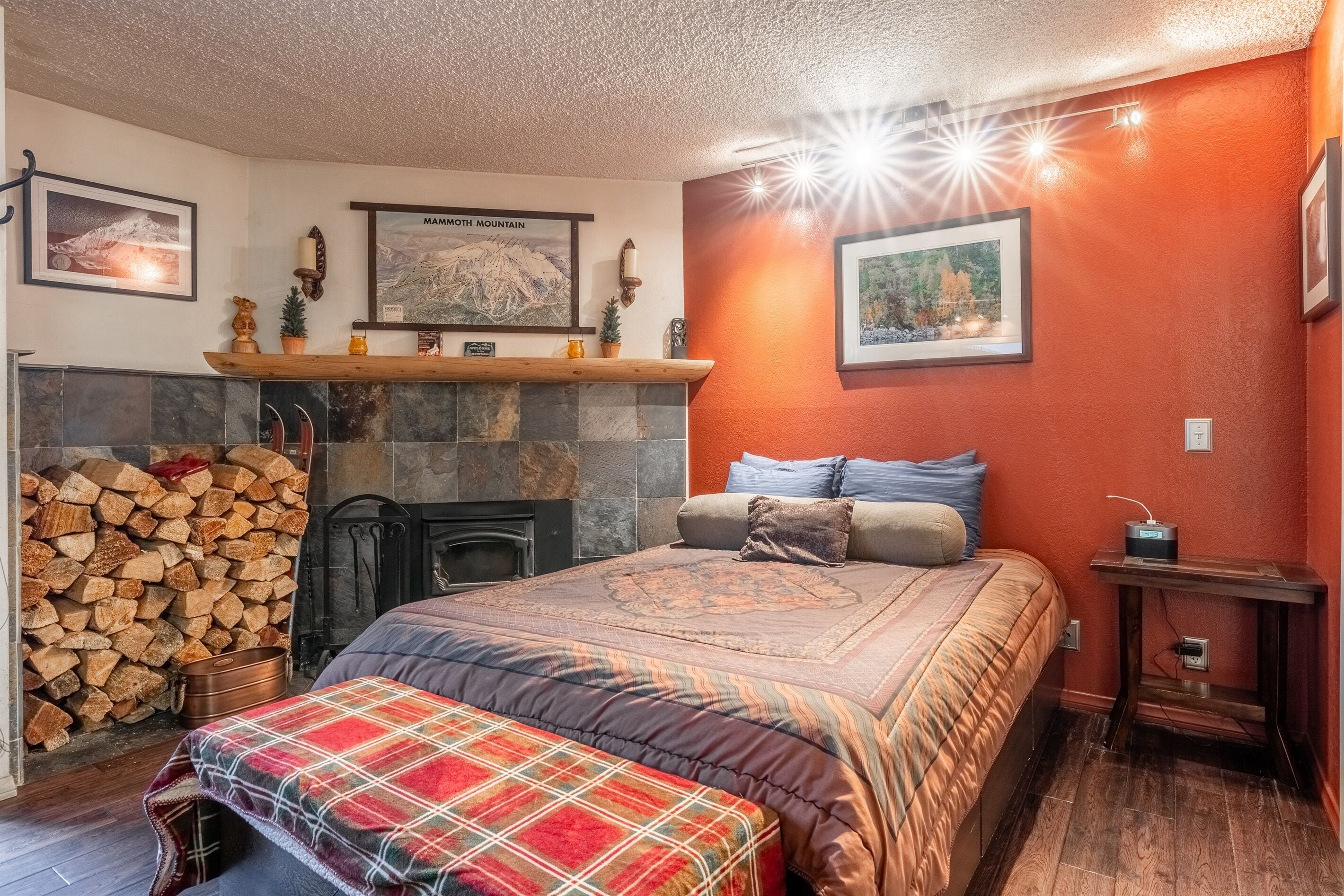 A cozy bedroom with a fireplace, a bed with a plaid bedspread, and a nightstand with a radio.
