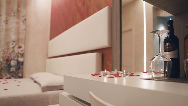 Een slaapkamer met een witte dressoir, een bed met bloemen gordijnen, en een fles wijn op het dressoir.