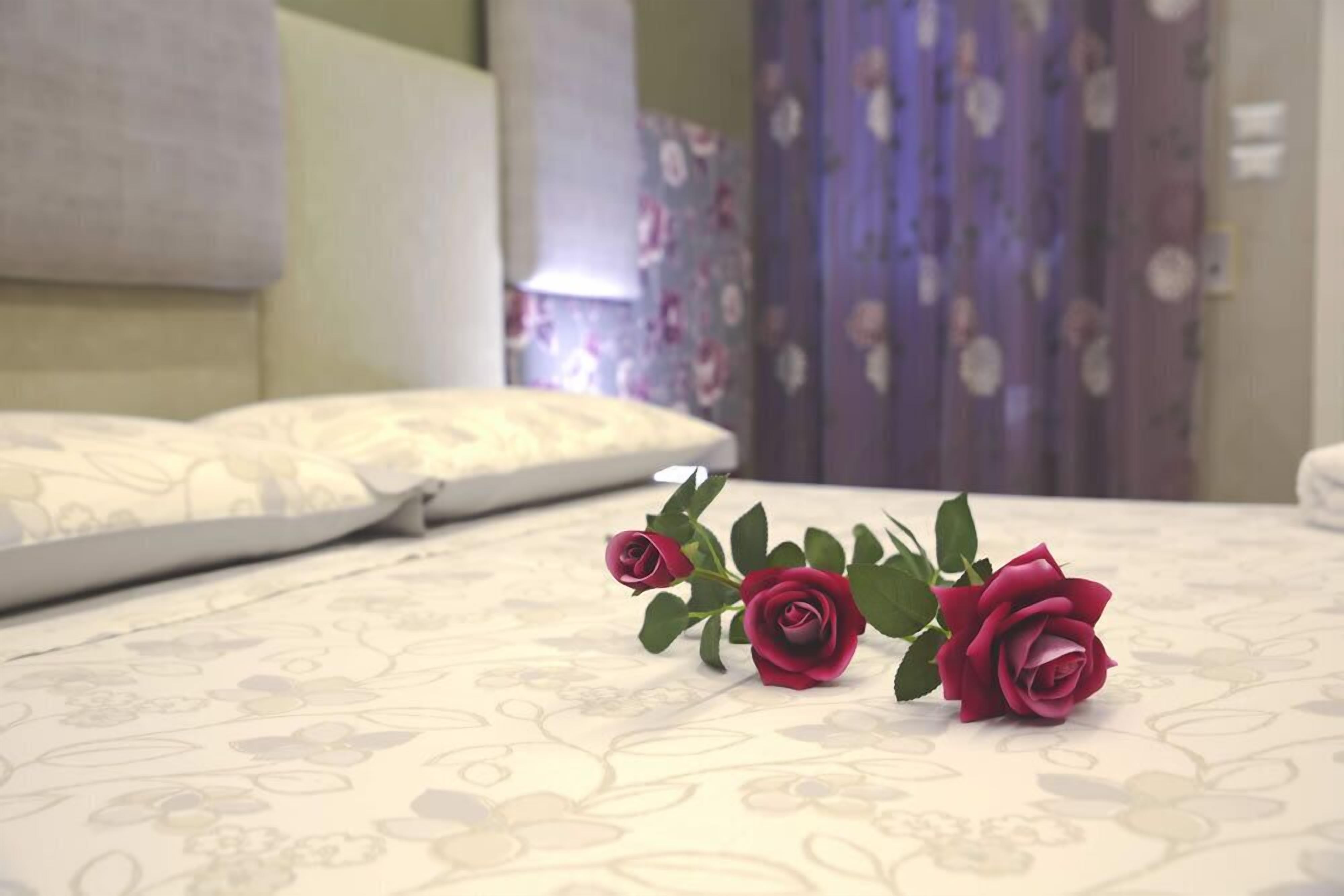 Una cama con ropa de cama de estampado floral y tres rosas rojas encima.