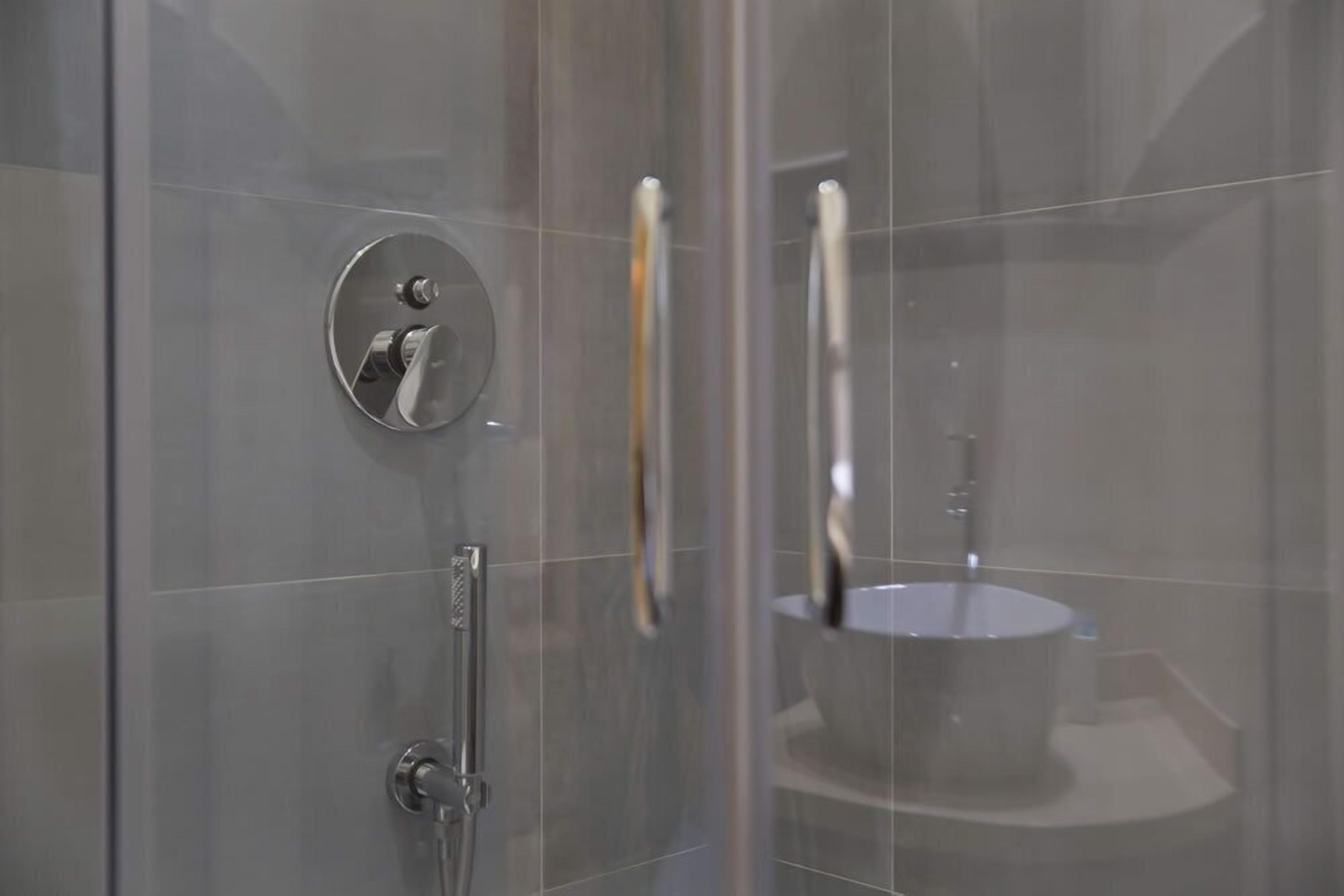 Ein modernes Badezimmer mit einer gläsernen Duschkabine, einem runden Spiegel und einem freistehenden Waschbecken.