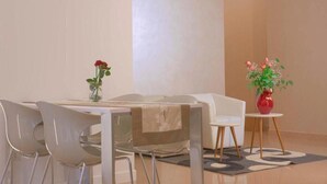 Een moderne eethoek met een witte tafel, stoelen en een bank. Op de tafel staan twee vazen met bloemen.