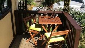 A wooden deck with a table and two chairs, a bottle of wine, and a glass on the table. - Charming Holiday Hideaway near the Lake (Lake Okareka)