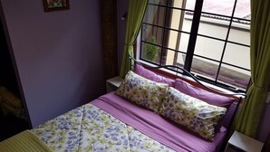 A single bed with a floral bedspread and a headboard, a nightstand, a window with a metal grid, and green curtains. - Charming Holiday Hideaway near the Lake (Lake Okareka)