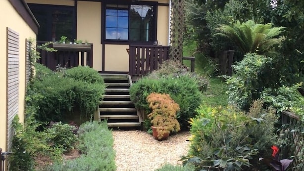 A garden with a wooden staircase leading to a house with a dark balcony. - Charming Holiday Hideaway near the Lake (Lake Okareka)