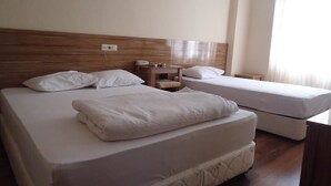 A hotel room with two beds, a wooden headboard, a bedside table with a lamp, and a window with curtains. - Hotel Ozkar (Mersin)