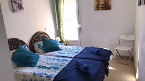 Ein Zimmer mit zwei Betten, einem Sessel, einem Fenster mit Vorhängen und einem Wandbild.