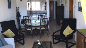 Ein Wohnzimmer mit einem Glastisch, zwei Sesseln, einer Couch und einem Essbereich mit Tisch und Stühlen.