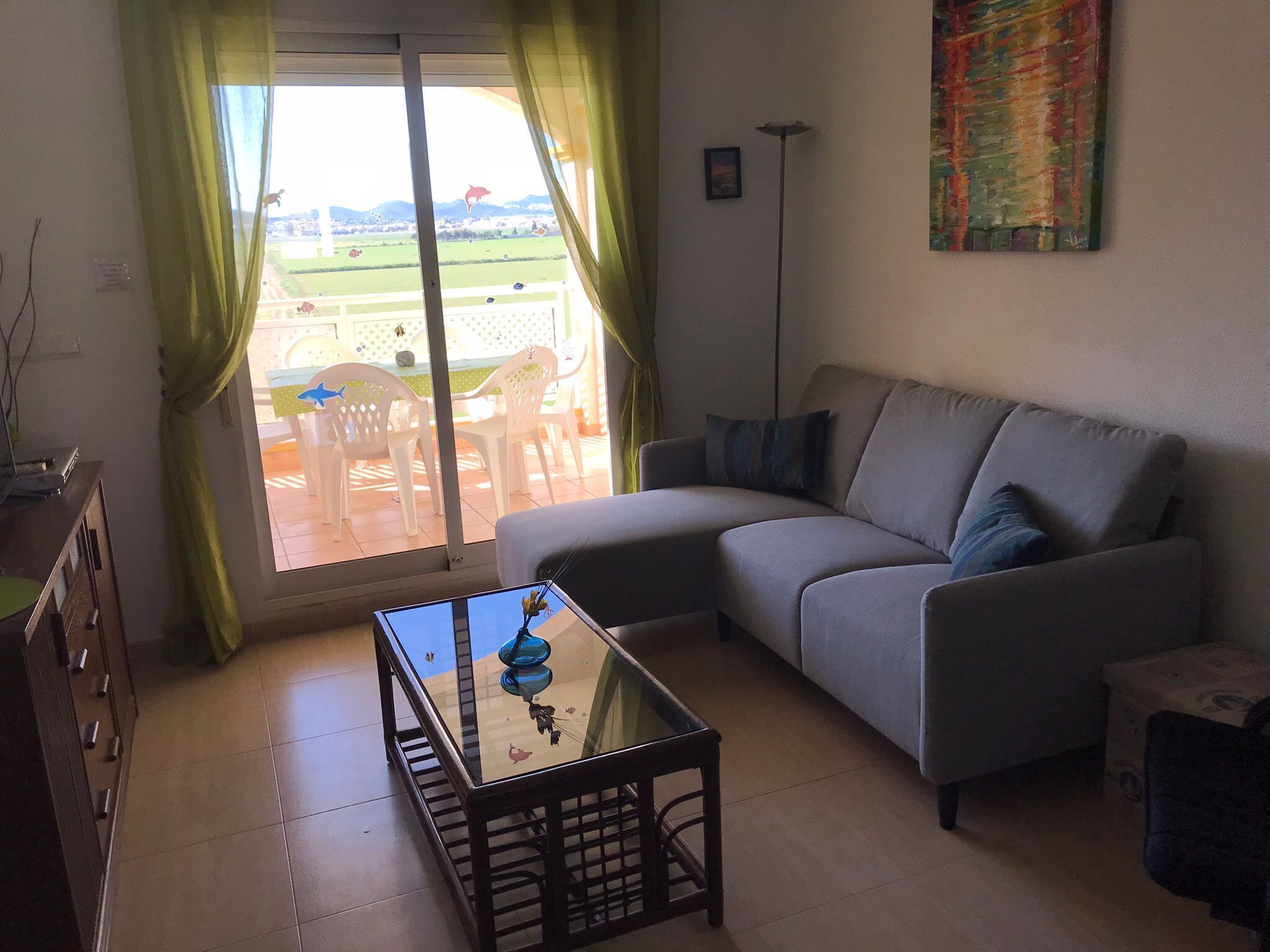A living room with a sofa, a glass coffee table, and a view of a garden through a sliding door.
