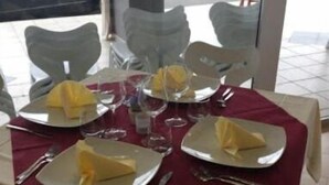 Mesa para cuatro personas con platos blancos, servilletas amarillas y cubiertos.